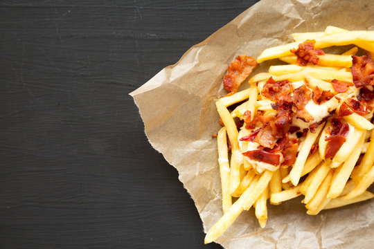 French Fries With Cheese Sauce And Bacon On A Black Background, Top View. Flat Lay, From Above, Overhead. Copy Space.