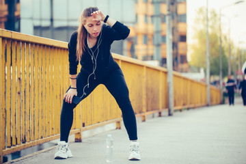 Young woman in black sports outfit resting after running on the bridge