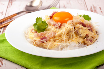 Traditional dish of Italian cuisine carbonara sauce with low-carb shirataka paste and egg yolk. Large portion served on a white plate. Close up and horizontal view.