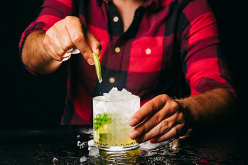 Bartender making Caipirinha cocktail on black counter and black background