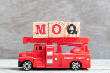 Red fire truck hold letter block in word MOQ (Abbreviation of Minimum Order Quantity) on wood background