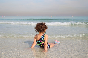 little adorable girl 2-3 years plays joyfully on the beach in sunset on holiday