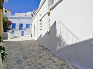 Beautiful peaceful stone paved empty alley, white houses with blue and yellow windows at noon time and fire hydrant Tinos island, Greece.