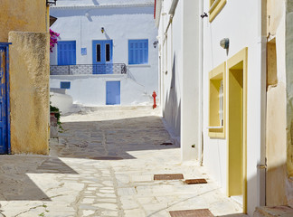 Beautiful peaceful stone paved empty alley, white houses with blue and yellow windows at noon time and fire hydrant Tinos island, Greece.