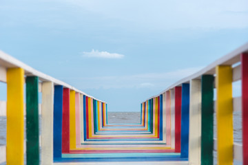 colorful rainbow wood bridge into the sea with blue sky background