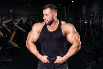 Fototapeta na wymiar Bodybuilder in the gym. Sports photo shoot. Man's fitness. Training and exercises with dumbbells. Men's photo shoot in low key. Athletic build.