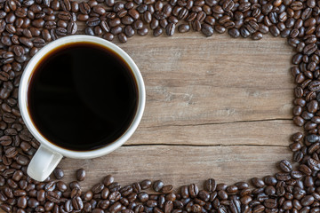 Black coffee in a white coffee cup and a coffee bean placed on an old wooden table. Top view