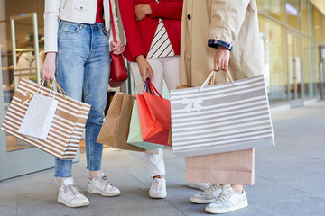 Close-up of unrecognizable stylish girls standing on street and holding paper bags with many purchases after shopping