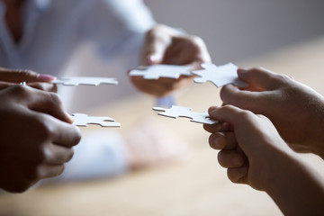 Close up members of multiracial team holding pieces of puzzle