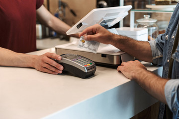 Photo of european man wearing paying debit card in cafe while waiter holding payment terminal - obrazy, fototapety, plakaty