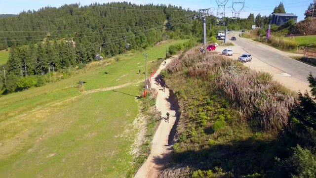 Aerial, reverse, drone shot of mountain bikers, downhill biking, on sand trail, on the slopes of a ski resort, in the french alps, at Lac Blanc bike park, in Massif des Vosges, Orbey, France