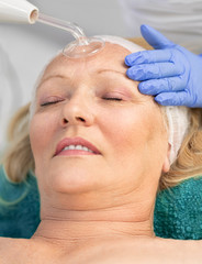 Obraz na płótnie Canvas Receiving electric darsonval facial massage procedure at beauty salon.