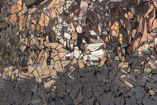 Cracked cement wall with dirty mosaic made from broken mirror pieces with distorted reflection in them.