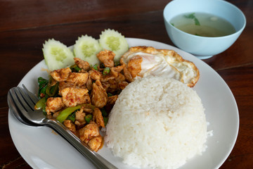 Rice and Stir fried chicken and curry paste with egg and soup on wood table.