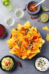 Nachos chips with melted cheese and dips variety in black bowl. Top view.