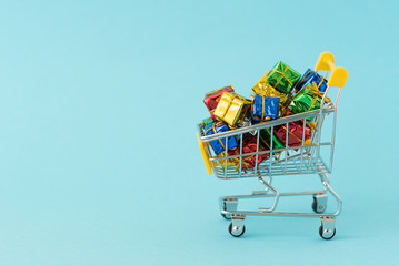 Christmas gifts in supermarket trolley on blue background . Online shopping concept - trolley cart full of presents. Black Friday and Ciber Mondey