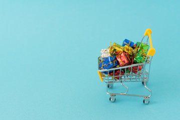 Christmas gifts in supermarket trolley on blue background . Online shopping concept - trolley cart full of presents. Black Friday and Ciber Mondey