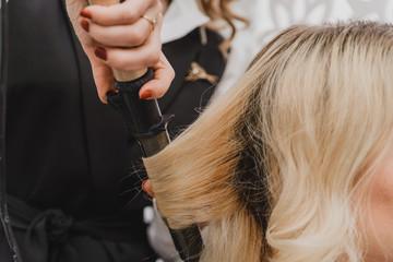 Fototapeta premium Stylist curling hair for young woman. Girl care about her hairstyle. to do curls