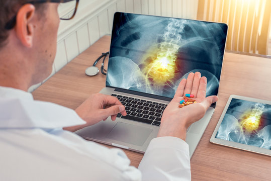 Doctor holding pills with x-ray of hips with pain in the spine on a laptop. Digital tablet on the wooden desk