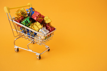 Christmas gifts in a supermarket trolley on yellow background. Online shopping concept - trolley full of gifts. Black Friday and Cyber Monday