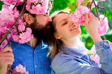 Obraz premium Couple spend time in spring garden. Happy family enjoying sunny day in park during cherry blossom season. Couple in sunny spring day. Man and woman in blooming garden. Couple stand near sakura tree.