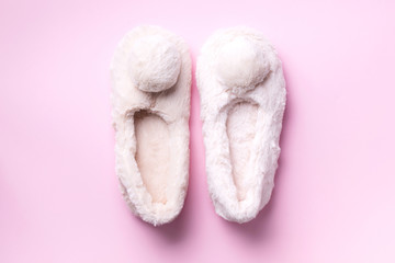 Nude fluffy home slippers with pompon on pastel pink background. Top view. Copy space. Cozy home footwear. Sweet home and spa, body treatment concept