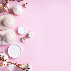 Bathroom accessories, nude fluffy home slippers, cotton flowers, candle, skin care products on pink background with copy space. Top view. Copy space. Spa and body treatment concept.