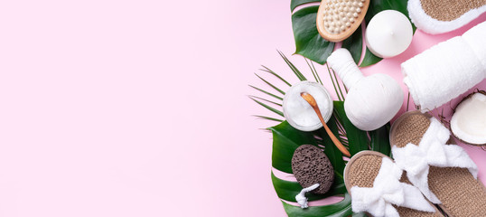 Spa tools: white towel, bamboo slippers, herbal ball, cream, wooden brush, coconut oil, monstera on pink background. Cosmetic products for body treatment. Beauty, relax and massage concept