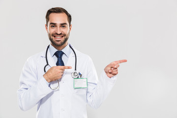 Portrait of joyful young medical doctor with stethoscope looking at camera and pointing fingers aside