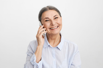 Attractive good looking mature European female on retirement spending hours on talking on smart phone to old friend using unlimited mobile package. Charming middle aged lady enjoying phone talk