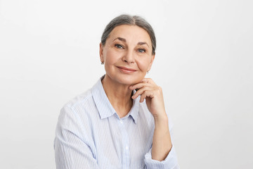 Elegant successful mature businesswoman in her sixties touching chin and smiling, having pensive...
