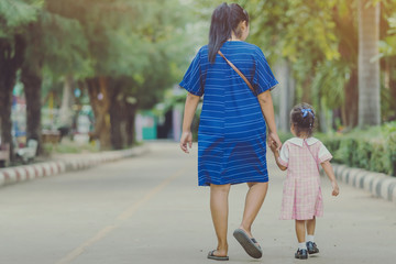 Mom and daughter pupil girl holding hand in hand on street go to the classroom together.