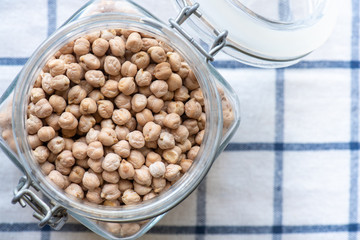 Uncooked dry chickpeas in a glass jar on white checkered tablecloths. Top view, copy space.