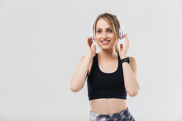 Image of happy blond woman 20s dressed in sportswear listening to music with headphones during workout in gym