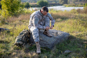 Soldier tying shoes. Soldier. Soldier in gear. The soldier sits and rests.	