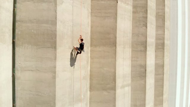 A young climber is moving up on a wall very fast. A building is very high. A day is nice and sunny.