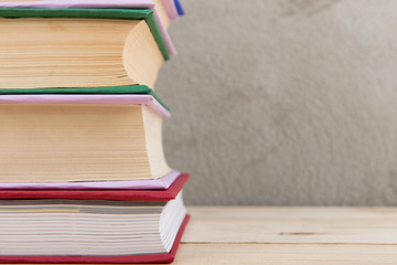 Education and reading concept - group of colorful books on the wooden table, concrete wall blackboard