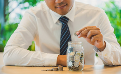 Businessman putting coins in glass. Saving money concept.