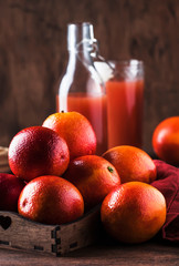 Juicy ripe shiny red bloody oranges in tray for making refreshing cocktail on rustic wooden table background, still life, selective focus