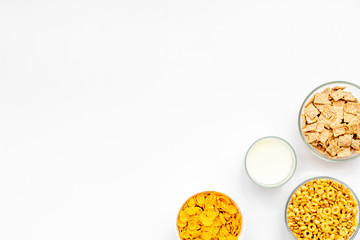 Various corn cereals in bowls and milk on white background top view copyspace
