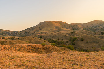 Hilly and mountainous steppe under the rays of the early sun with yellowed dry grass