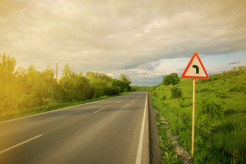  Empty road with sign preventive repair of the road, blue sky with clouds and green trees with a sun ray 