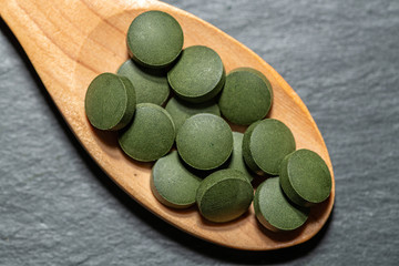 Spirulina,chlorella supplement pills in wooden spoon . Selective focus