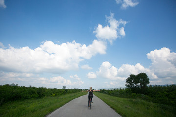 Obraz premium Young beautiful woman riding bicycle and spreading arms in countryside.