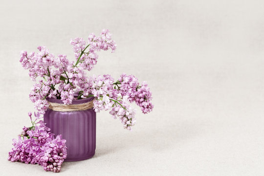 Vase with bouquet of lilac flowers on blurred background. Rustic style. Selective focus.