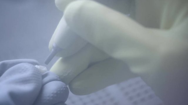 Dental technician polishing artificial ceramic teeth using sandblaster in the dental lab. Professional wearing gloves while holding fake teeth in hand and polishing it with sand blaster