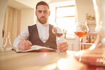 Portrait of professional sommelier looking away pensively during wine tasting session in winery lit by sunlight, copy space