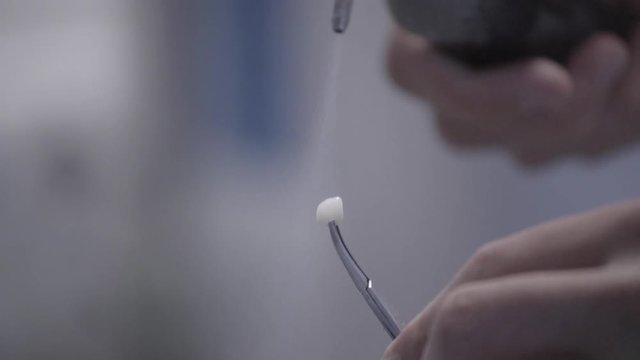 Dental technician polishing artificial ceramic teeth using compressed air blaster in the dental lab. Professional holding fake teeth and polishing it with air blaster