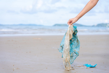 Woman’s hand picking up used plastic bag on sand beach, cleaning seaside beach.  Environmental...