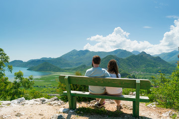 couple sits on a bench and admires the view of the lake and hills